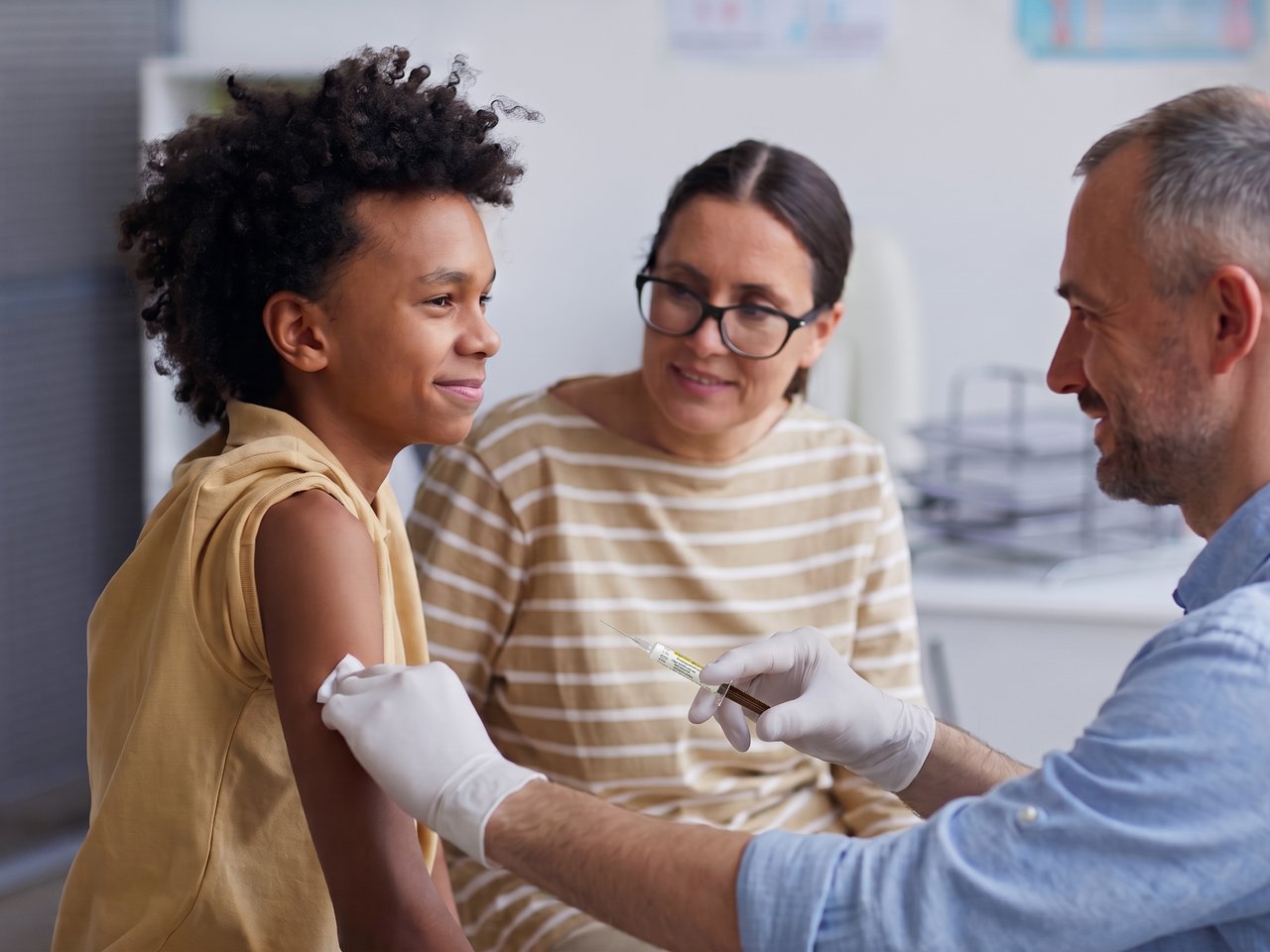 Un adolescent reçoit un vaccin dans le bras, en présence d’une femme et d’un médecin